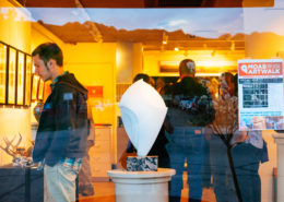 Picture of sculpture in a window of a gallery with people inside