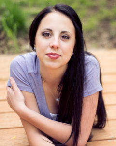 Girl with black hair laying on her stomach while wearing a blue shirt and looking at the camera