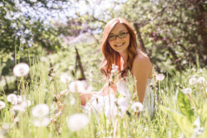 Girl wearing glasses and smiling while sitting in a field