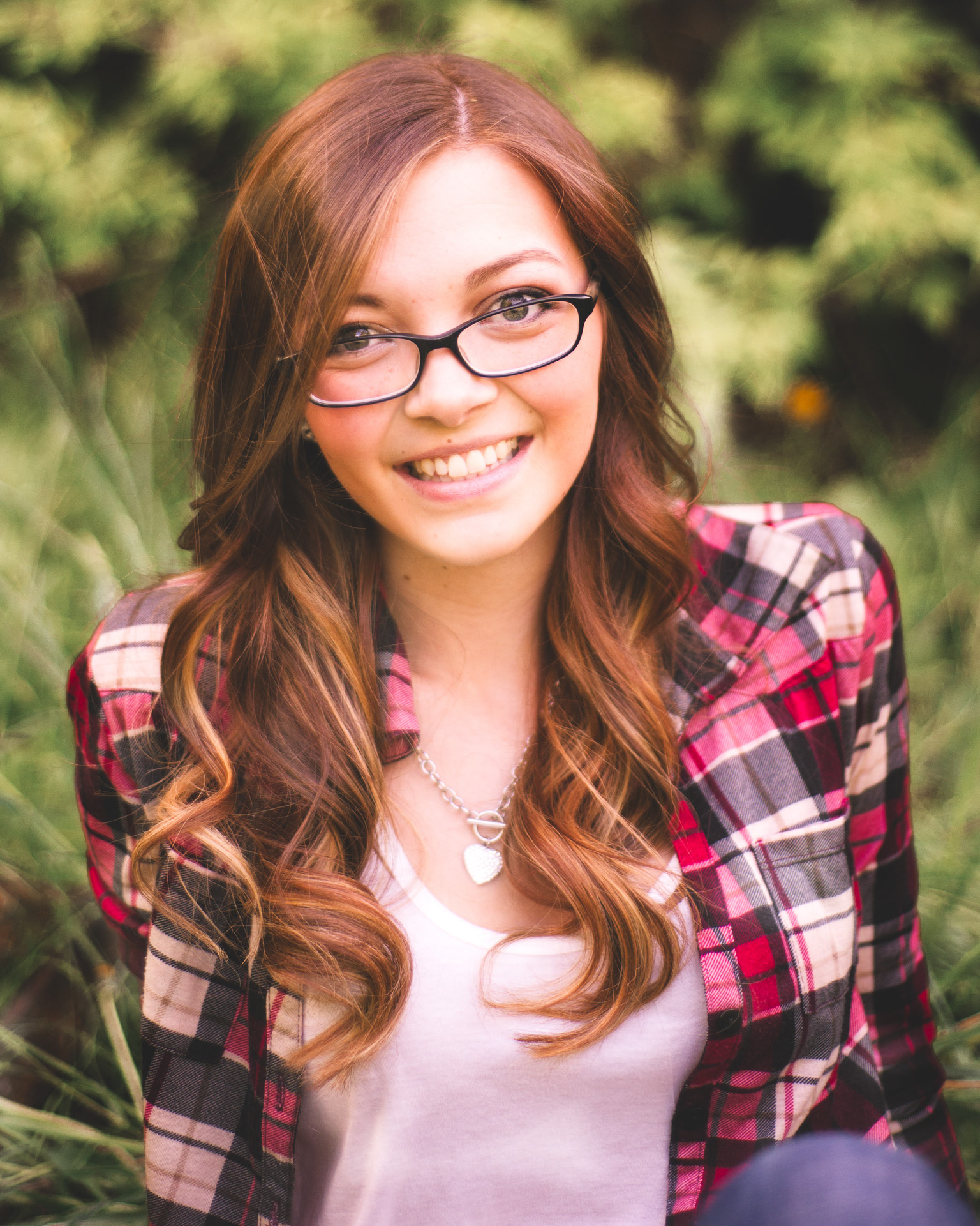 girl in glasses wearing a red plaid shirt with foliage in the background