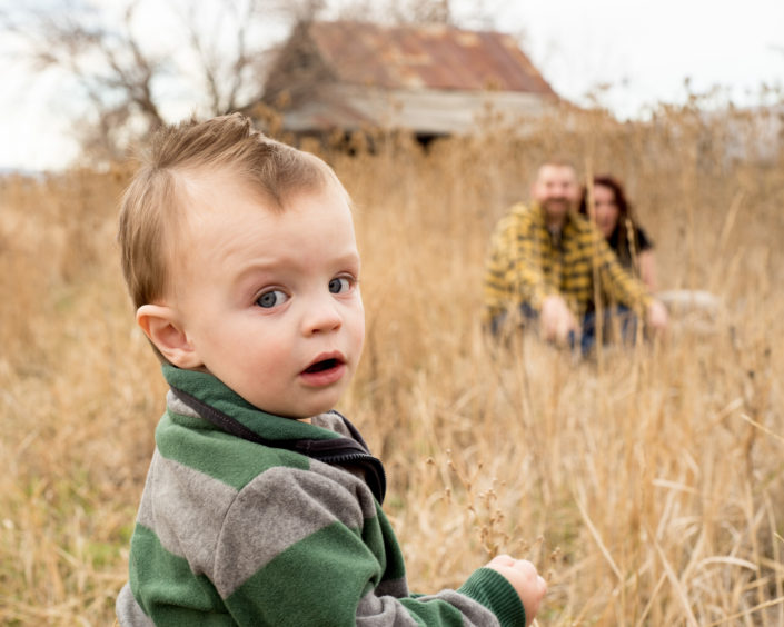 Portrait, Moss Image, MOab Photographer, picture of a boy looking back at the camera with his mom and dad sitting in the background surrounded by yellow grass