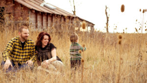 Moss Image, Portrait, Moab Photographer, picture of a mom and dad sitting in front of a barn watching their son play