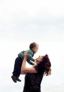 Picture of a mom holding her son up to her face with the sky as a background
